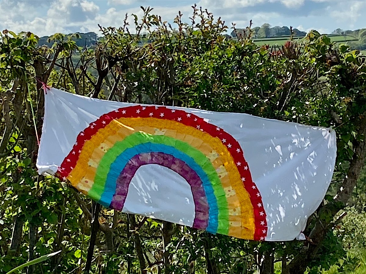 A rainbow painted onto a sheet and hung on a hedge